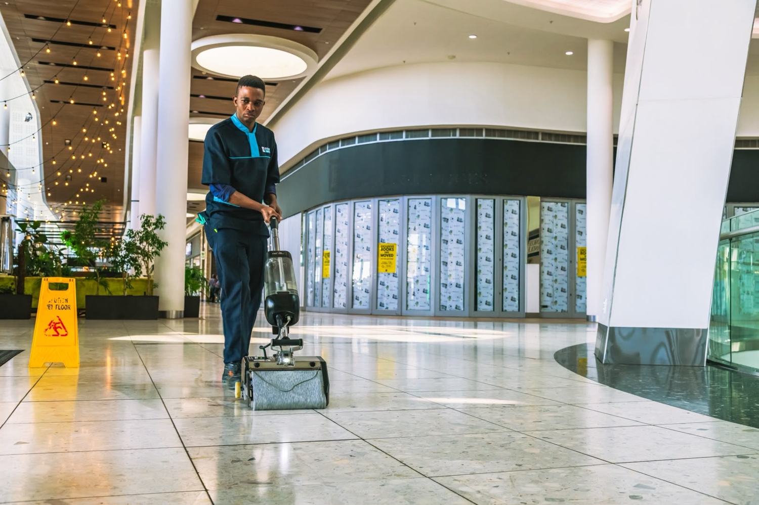 Bidvest Prestige colleague cleaning a mall floor beside a wet floor sign