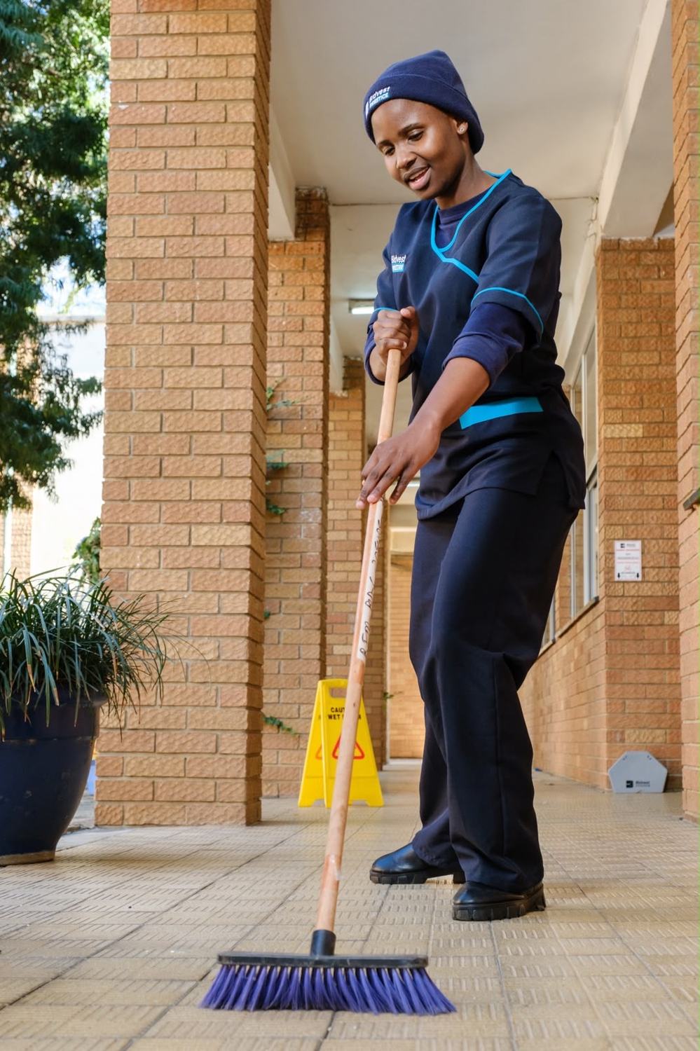 Smiling Bidvest Prestige colleague sweeping a walkway
